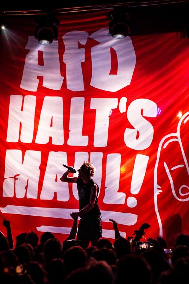 Protestveranstaltung mit rote Flagge und dem Slogan „AFD HALT'S MAUL!“ im Hintergrund.