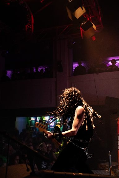 Musiker mit lockigem Haar spielt Gitarre auf einer Bühne in einem Club.