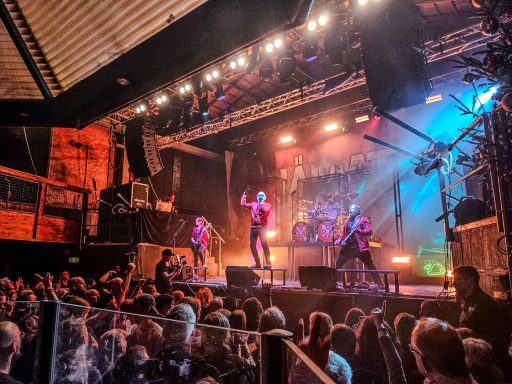 Ein Livekonzert mit einer Band auf der Bühne und begeistertem Publikum davor.