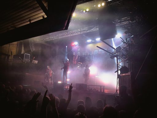 Live-Musikaufführung auf einer Bühne mit Lichtern und Nebel, Publikum voller Energie.