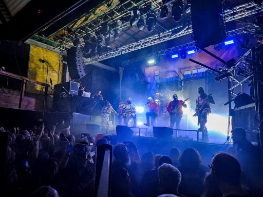 Bandperformanz auf einer Bühne mit Lichtern, vor begeistertem Publikum.