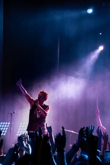 Ein Sänger auf der Bühne, umgeben von begeisterten Fans mit erhobenen Händen.