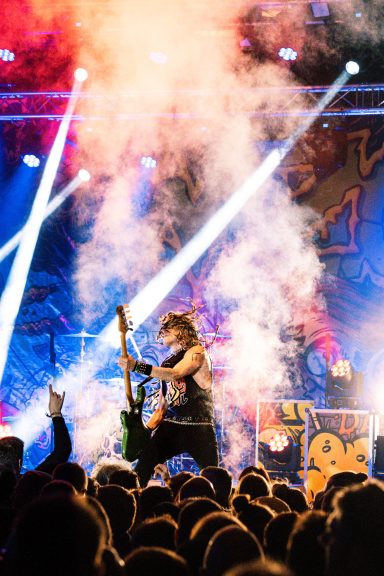 Musiker spielt E-Gitarre auf einer Bühne mit bunten Lichtern und Nebel.