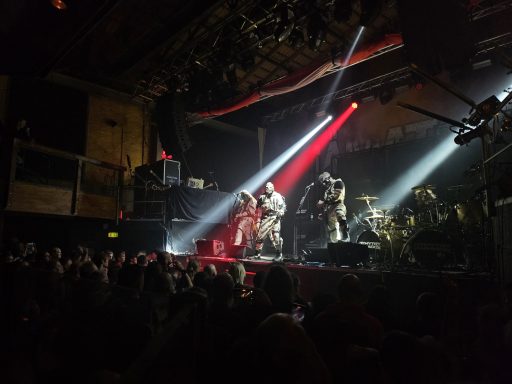 Liveband auf der Bühne mit Lichtern und Menschenmenge im Hintergrund.