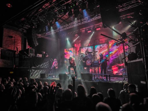 Musikband beim Auftritt auf einer Bühne mit bunten Lichtern und Publikum.