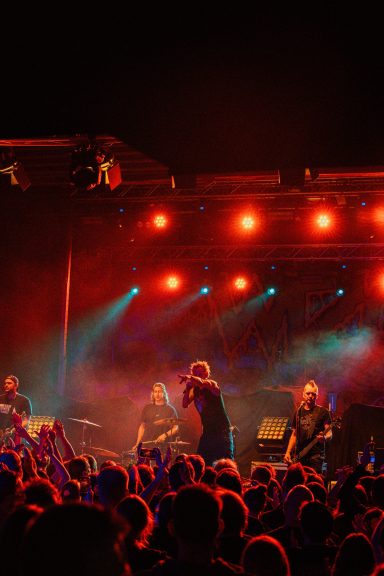 Band spielt auf einer Bühne, umgeben von begeistertem Publikum und bunten Lichtern.