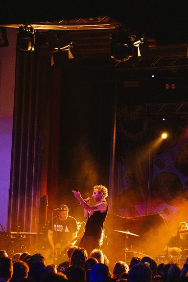 Bühne mit einem Sänger und Musikern, beleuchtet von bunten Lichtern vor Publikum.